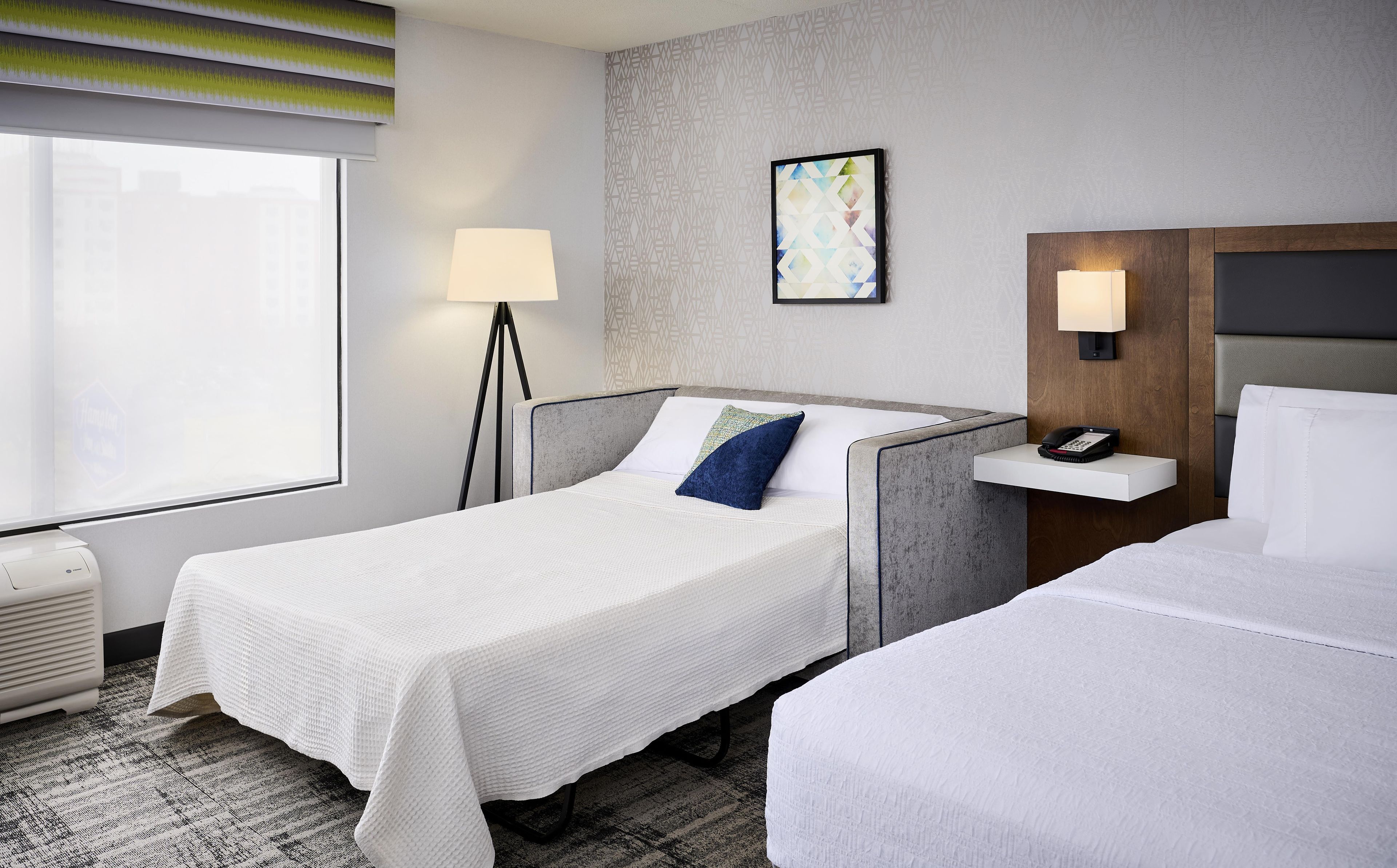 A hotel room with a single bed, a bedside table with a phone, a lamp, and a painting on the wall.