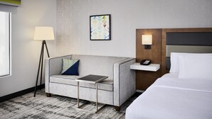 A hotel room with a sofa, a small table, a bedside table with a phone, a lamp, and a bed. - Hampton Inn & Suites by Hilton Windsor (Windsor)