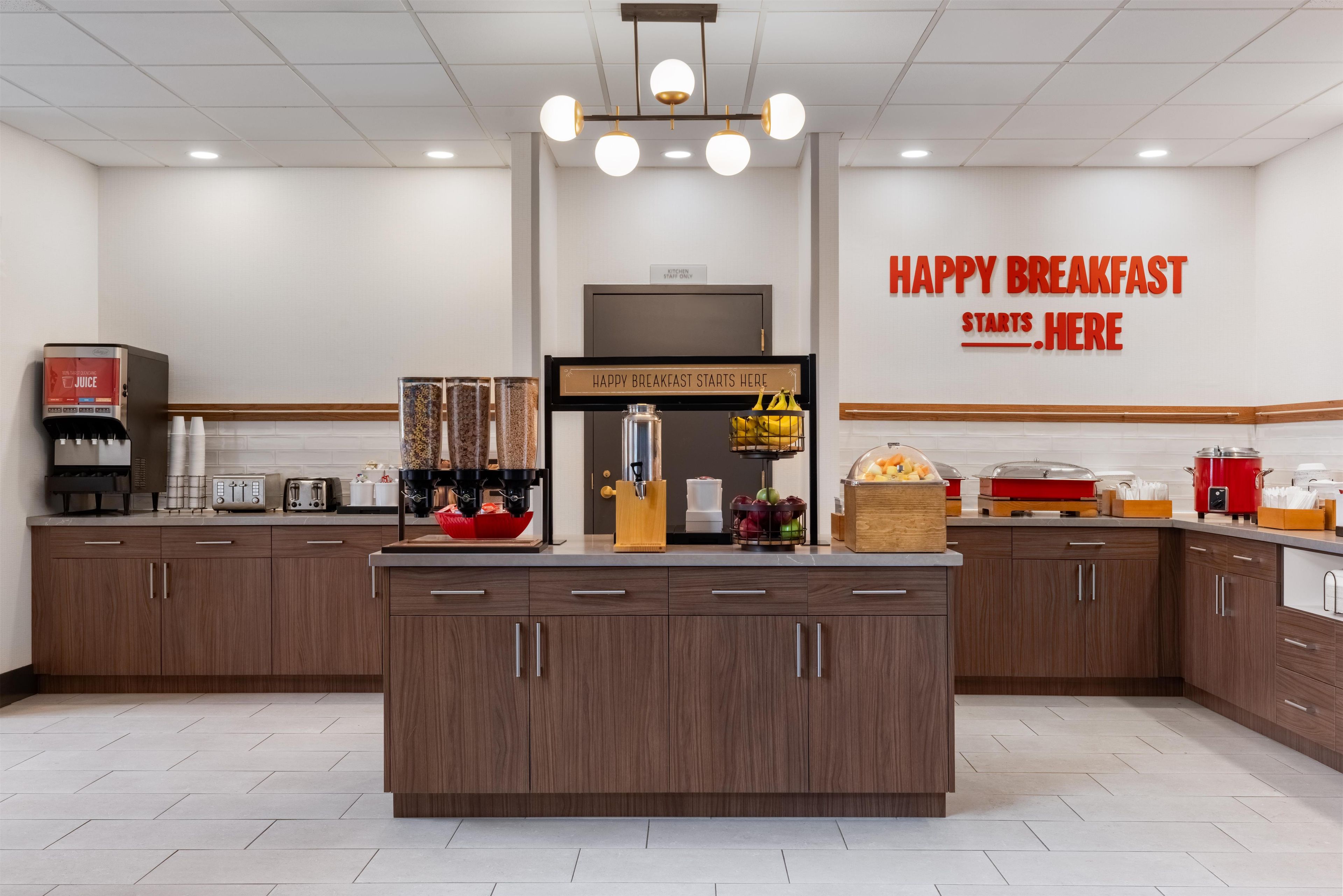 A modern kitchen with a central island, a coffee machine, a juice dispenser, and a breakfast sign.