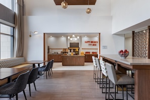 A modern dining area with a central island, seating arrangements, and a kitchen in the background.
