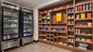 Un espace dédié à la présentation des collations et des boissons, équipé de distributeurs de boissons réfrigérés et d’étagères remplies de diverses collations et de produits emballés.