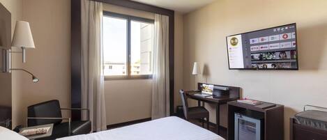 Hotelkamer met een bed, bureau, stoel, lamp en een televisie waarop een B&B-bord staat.