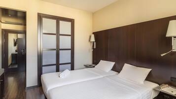 Una habitación de hotel con una cama grande, un armario de madera, un escritorio con lámpara y un espejo.