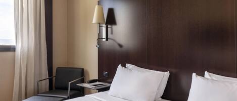 A hotel room with a large bed, a desk with a lamp, a chair, and a view of the outdoors.