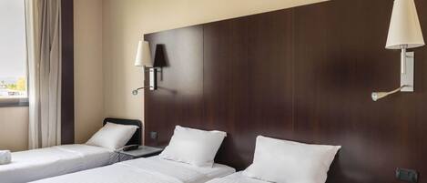 Una habitación de hotel con dos camas, una mesita de noche con lámpara y una ventana con cortinas.