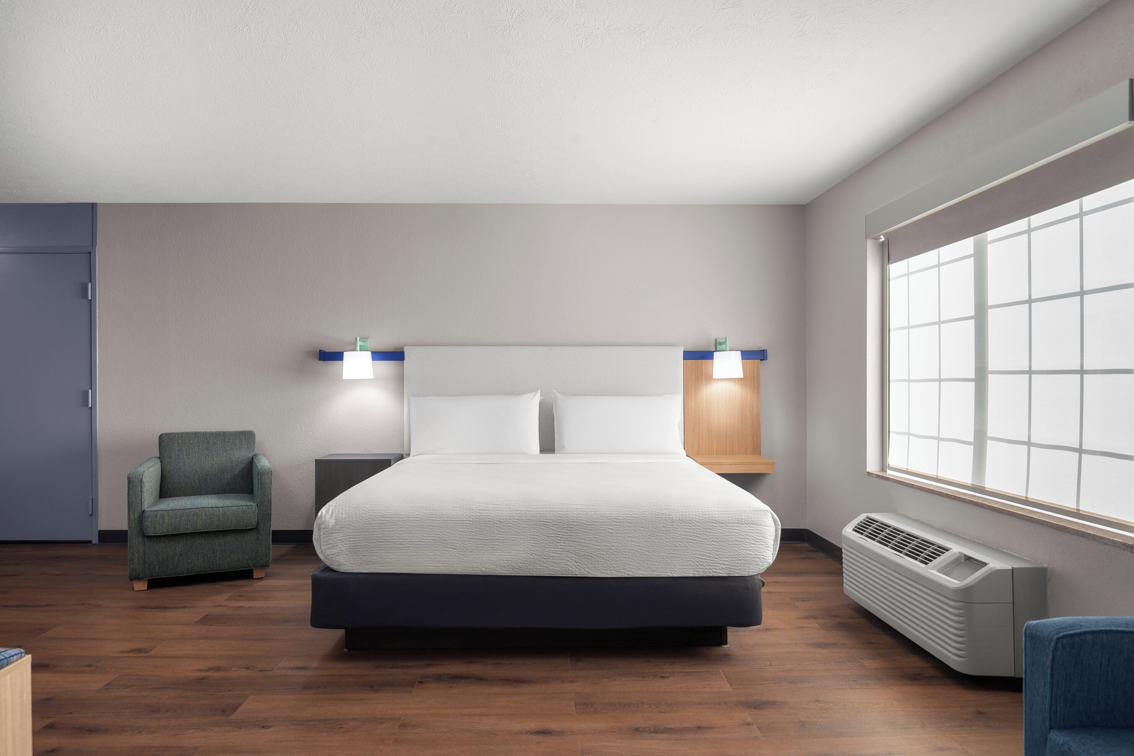 Una habitación de hotel moderna con una cama grande, una silla, una mesita de noche y una ventana con persianas.