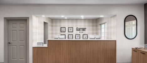 Zona de recepción de un hotel con un mostrador de madera, obras de arte enmarcadas y un letrero que dice 'Garner ANIHG HOTEL'.