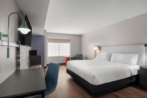 A modern hotel room with a bed, desk, chair, and a television.