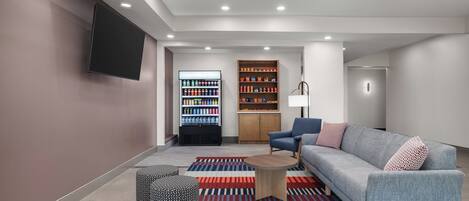 A modern lounge area with a sofa, a coffee table, patterned ottomans, a beverage fridge, and a cabinet.
