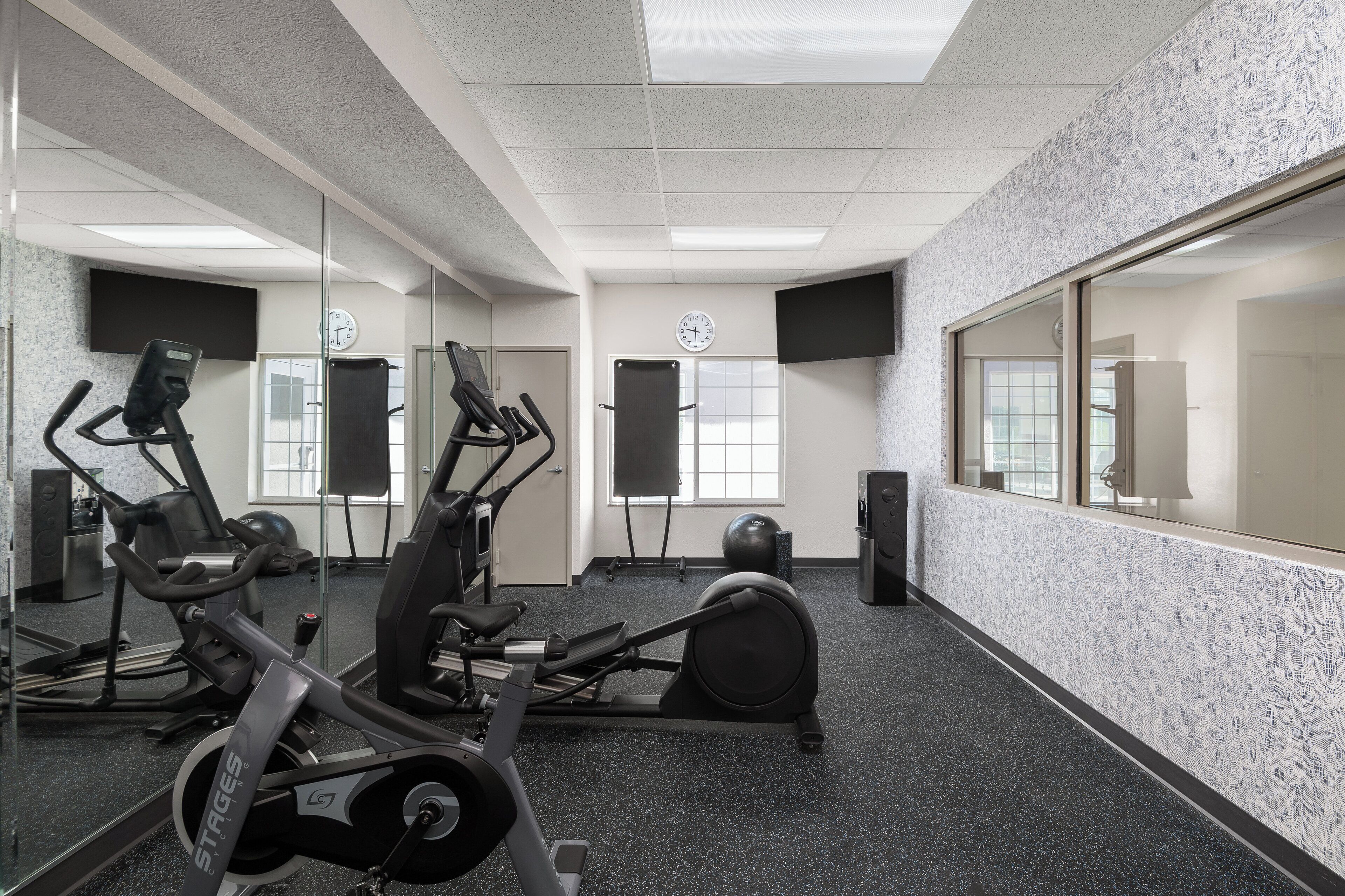 Uma academia com equipamentos de exercícios, espelhos e um relógio na parede.