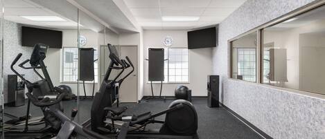 Uma academia com equipamentos de exercícios, espelhos e um relógio na parede.
