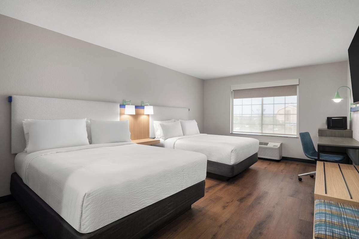 Une chambre d’hôtel avec deux lits, un bureau, une chaise et une fenêtre.