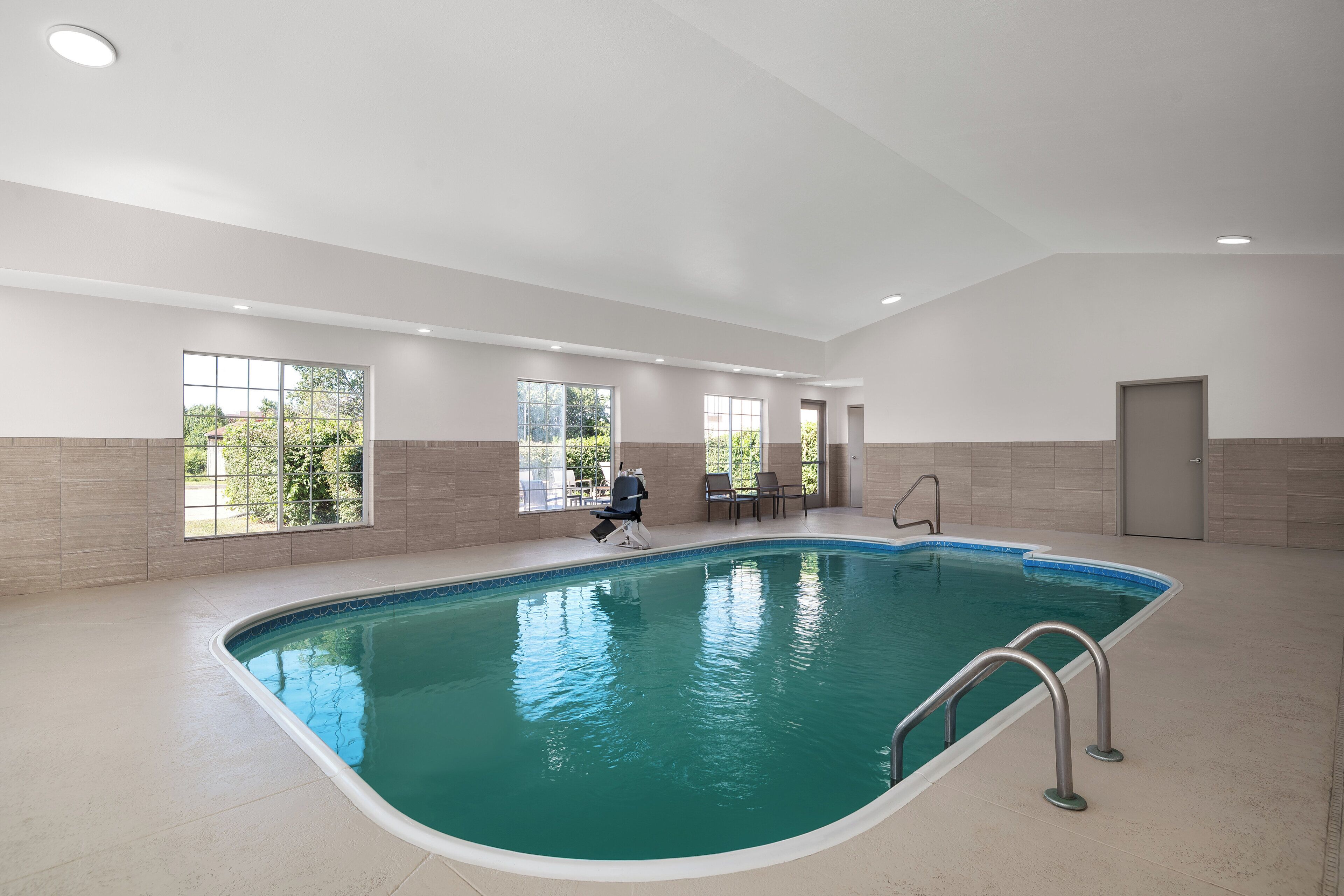 Una piscina interior con agua cristalina, rodeada de amplios ventanales y un suelo de baldosas.