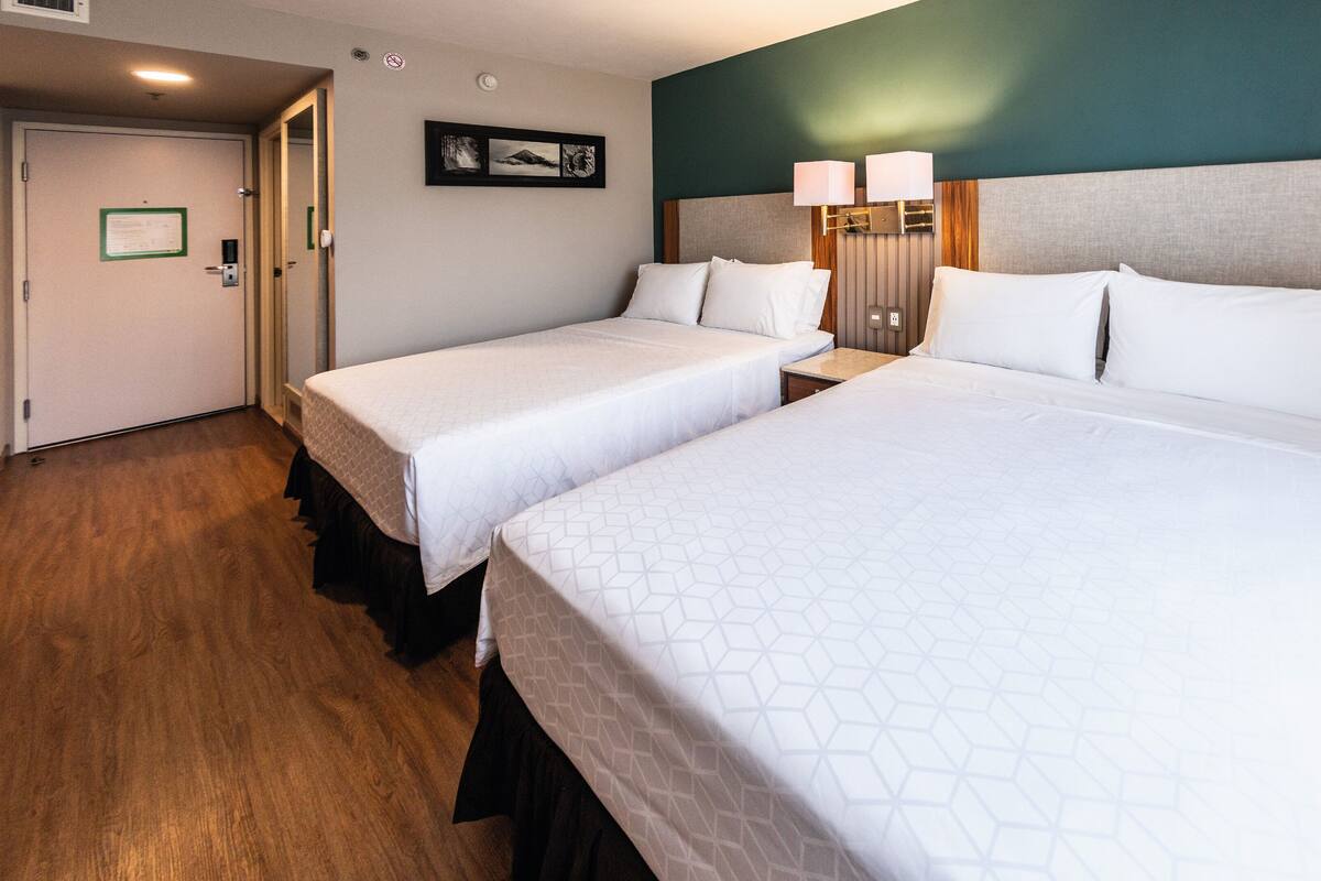 A hotel room with two single beds and one double bed, wooden flooring, a green accent wall, and a framed picture on the wall.