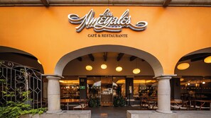 El exterior del Café & Restaurante Los Nmeyales, con una fachada naranja cálida, entrada en arco y lámparas colgantes.