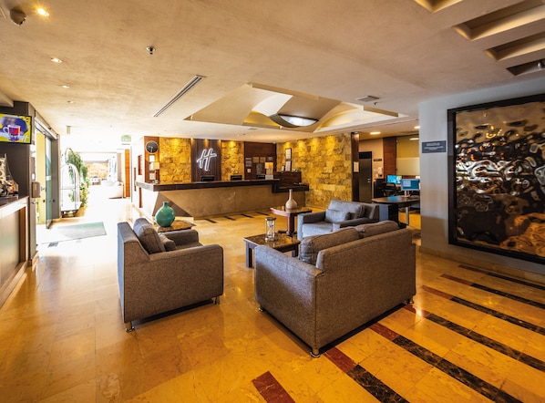 Un vestíbulo de hotel con una recepción, zona de estar y una obra de arte grande en la pared.