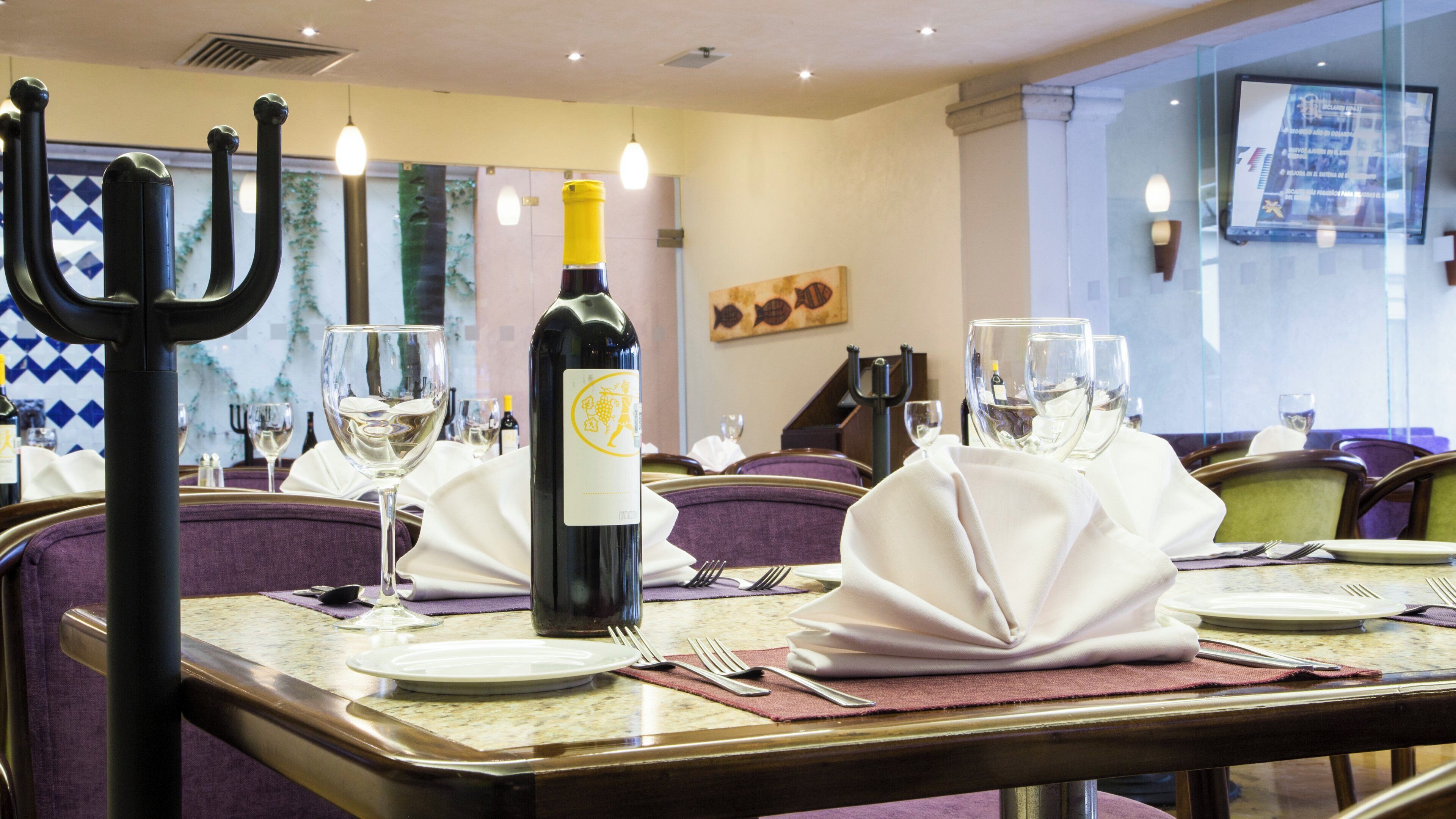 A restaurant dining area with tables set for two, featuring a bottle of wine, wine glasses, and a menorah.