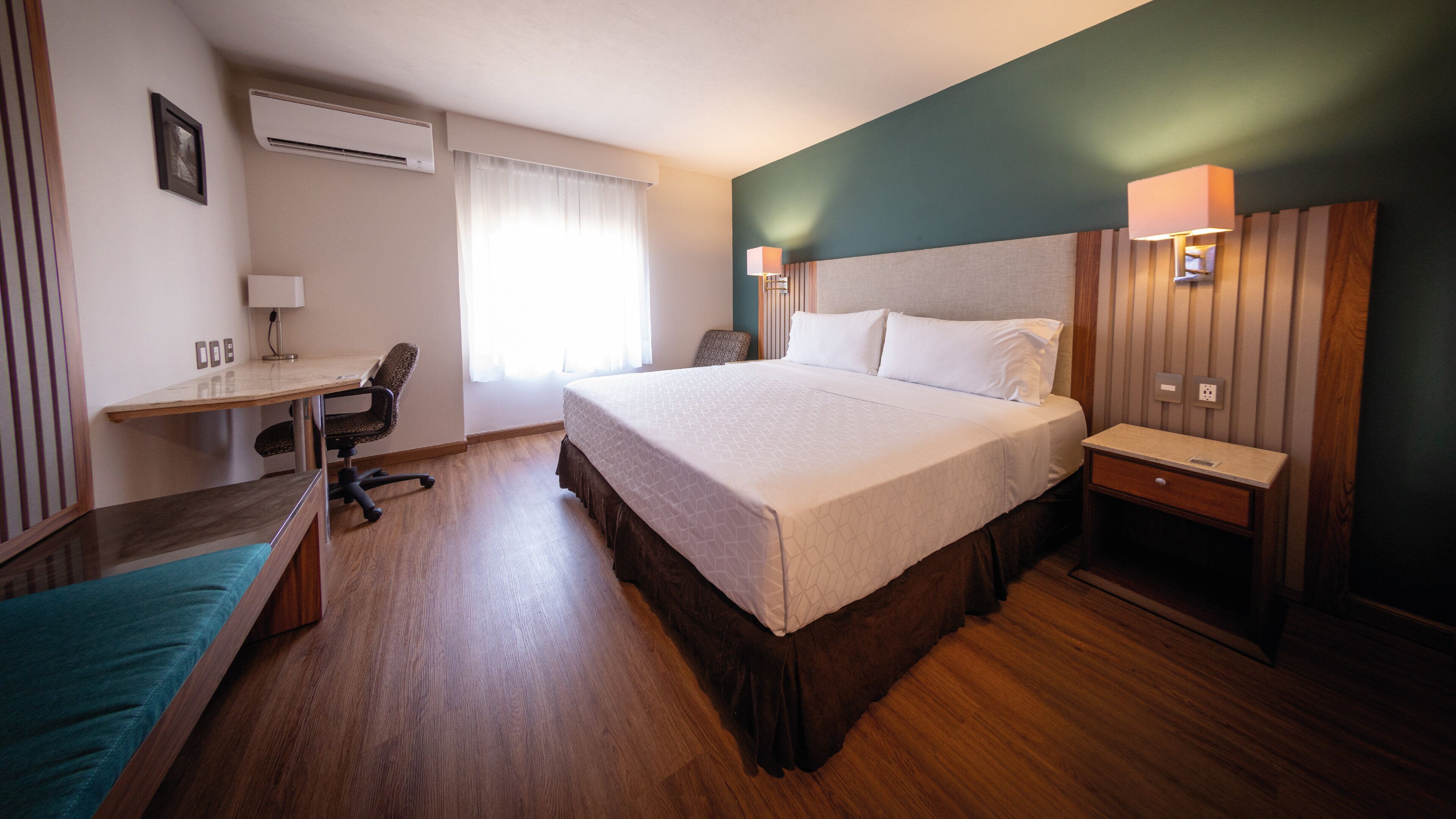 A hotel room with a bed, desk, chair, and a small seating area.