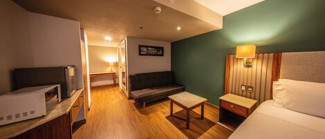 A hotel room with a bed, a desk, a sofa, and a microwave.