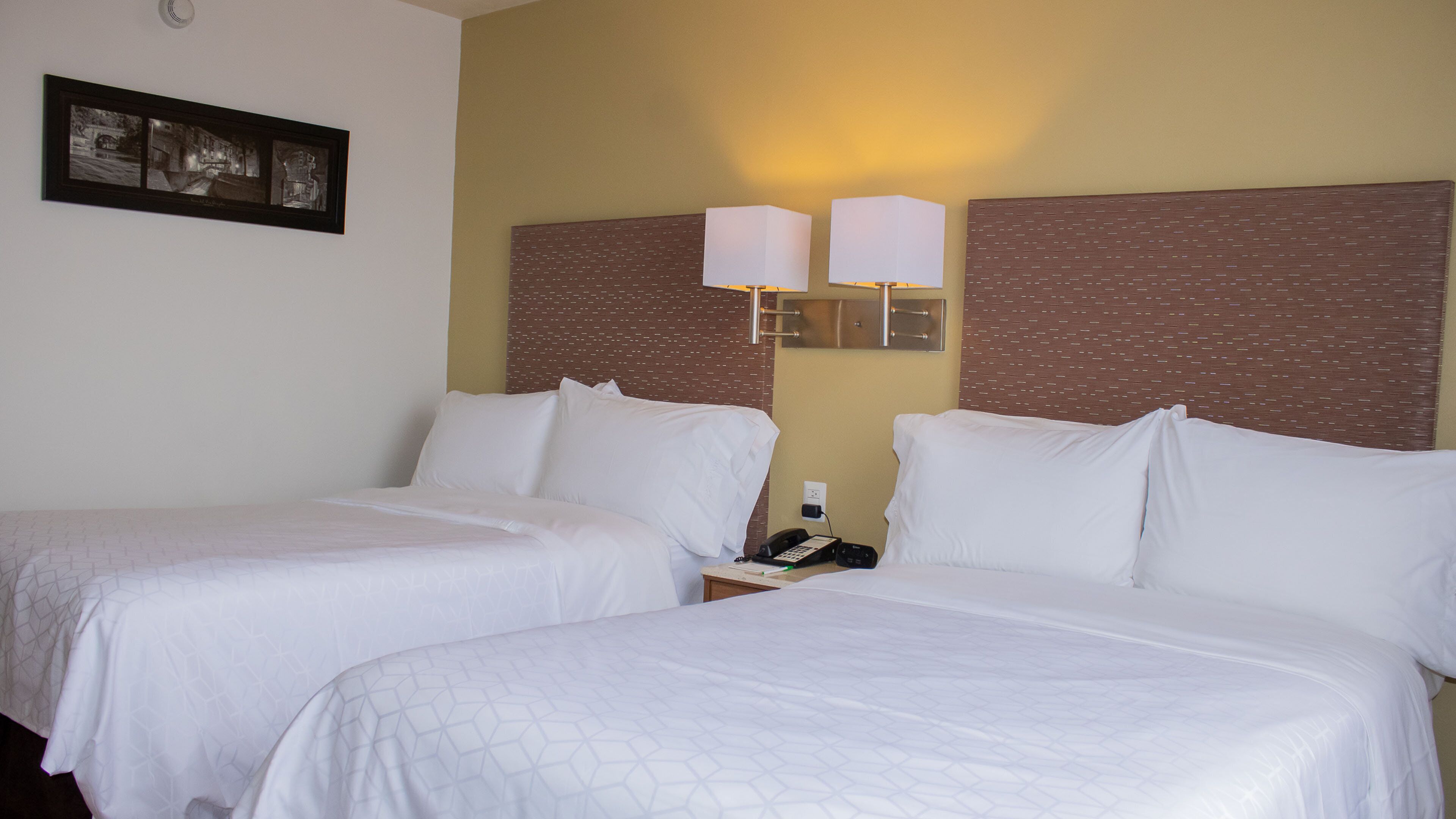 A hotel room with two beds, a nightstand, a telephone, and a wall-mounted lamp.