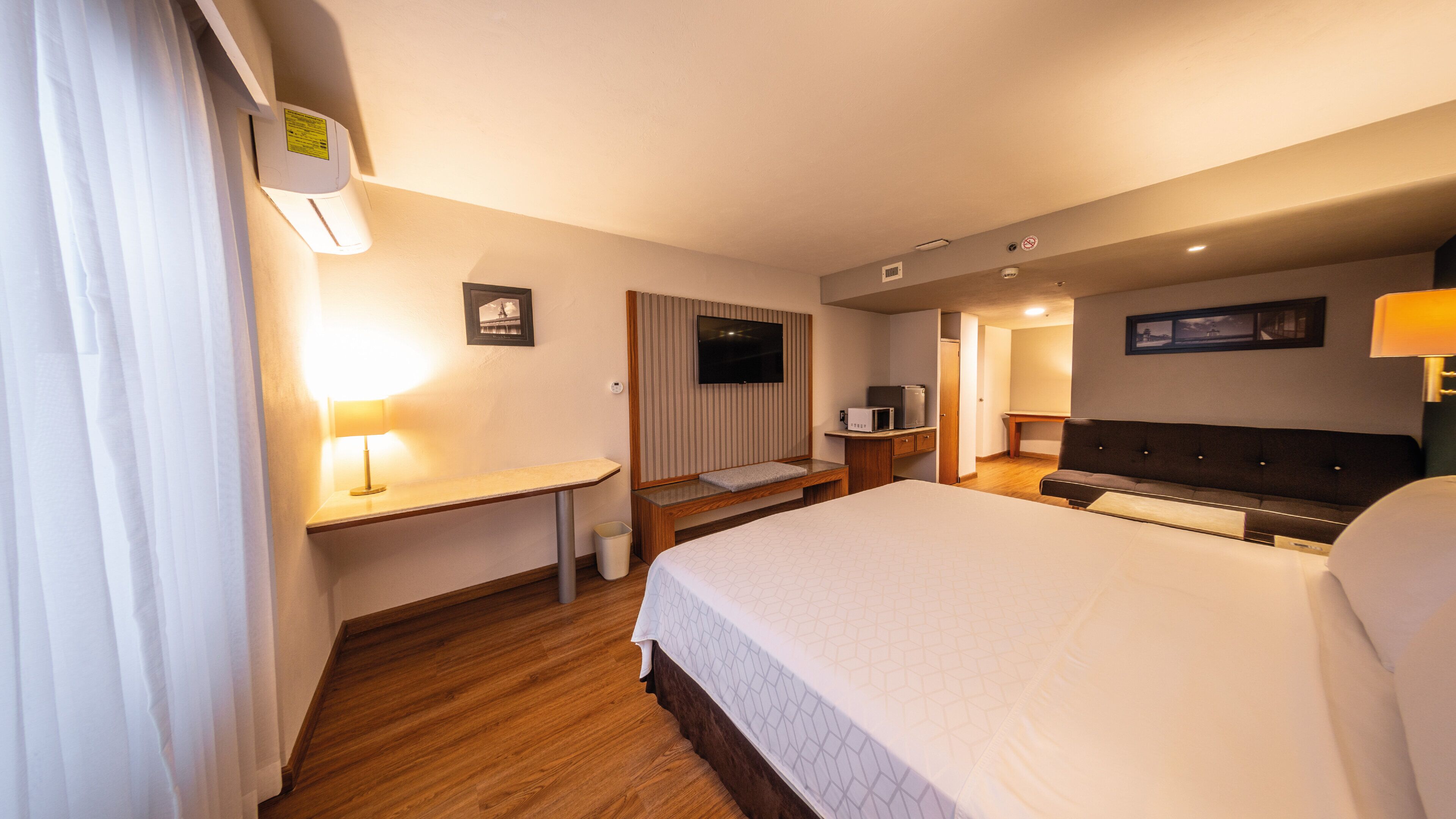 Une chambre d’hôtel avec un grand lit, un bureau avec une lampe, une télévision et une petite kitchenette.