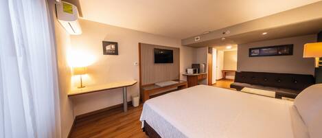 Une chambre d’hôtel avec un grand lit, un bureau avec une lampe, une télévision et une petite kitchenette.