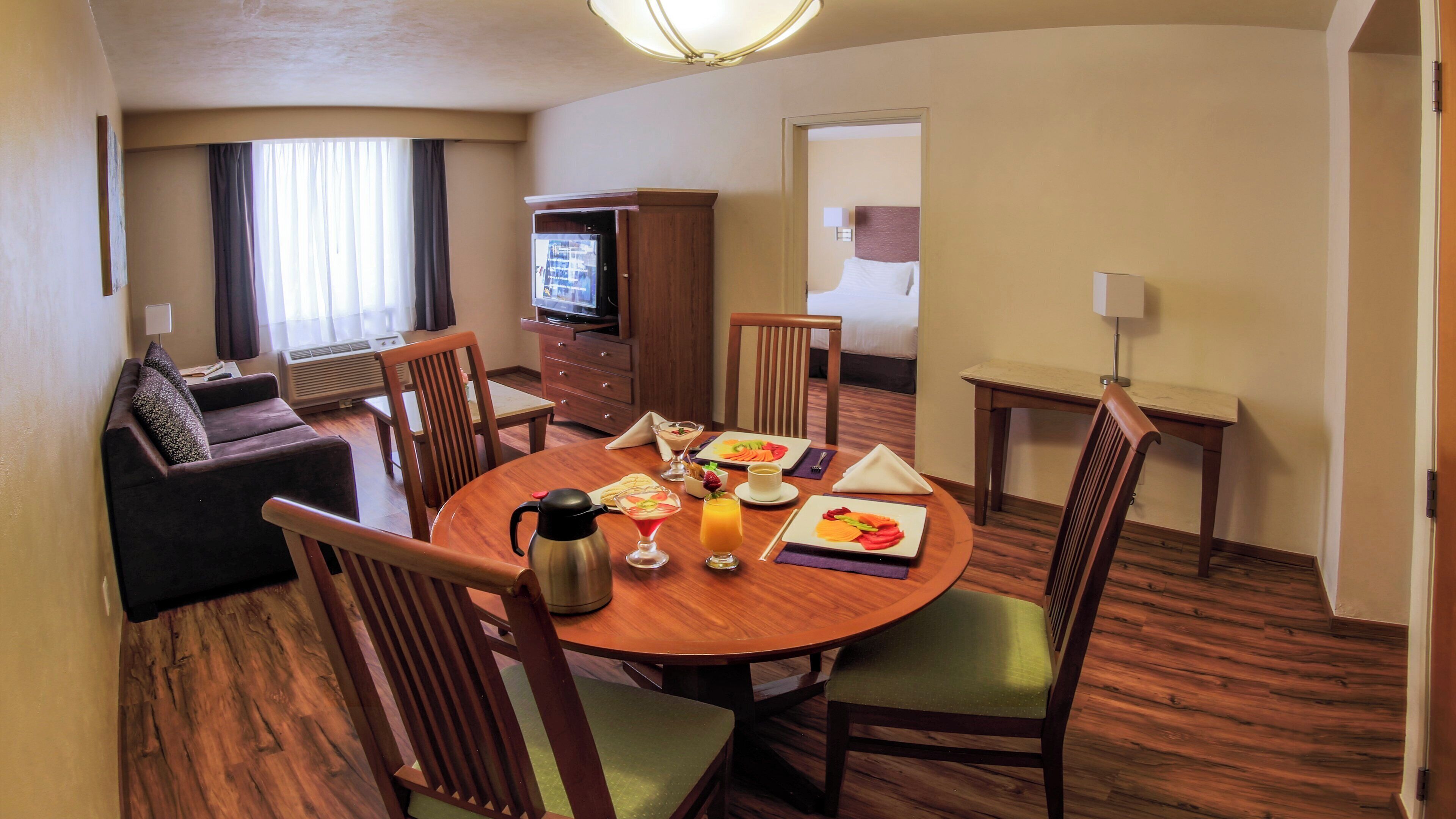 A hotel room with a dining area, a sofa, a TV, and a bed.