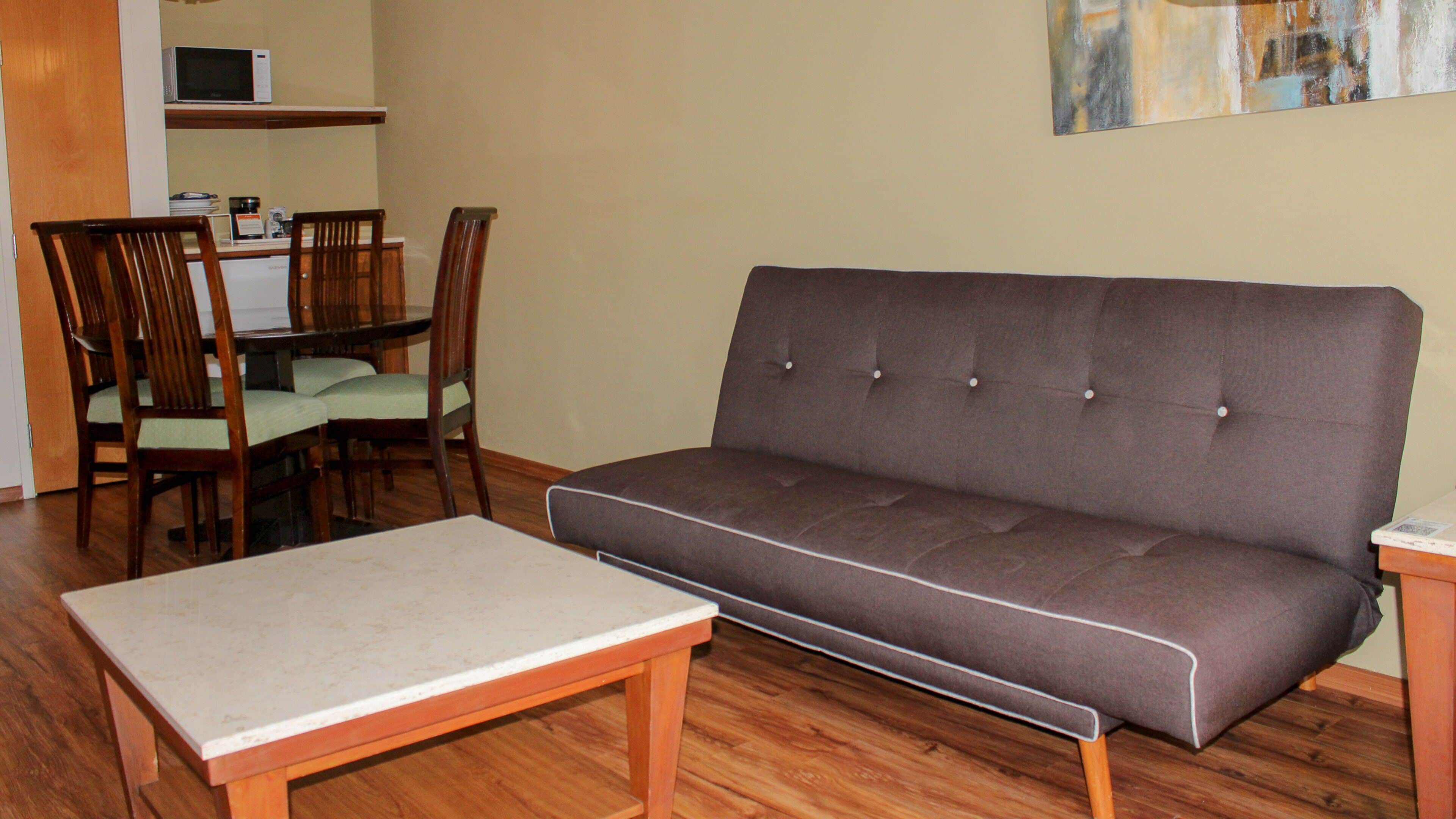 A living room with a sofa, a small table, and a dining area with chairs and a microwave.