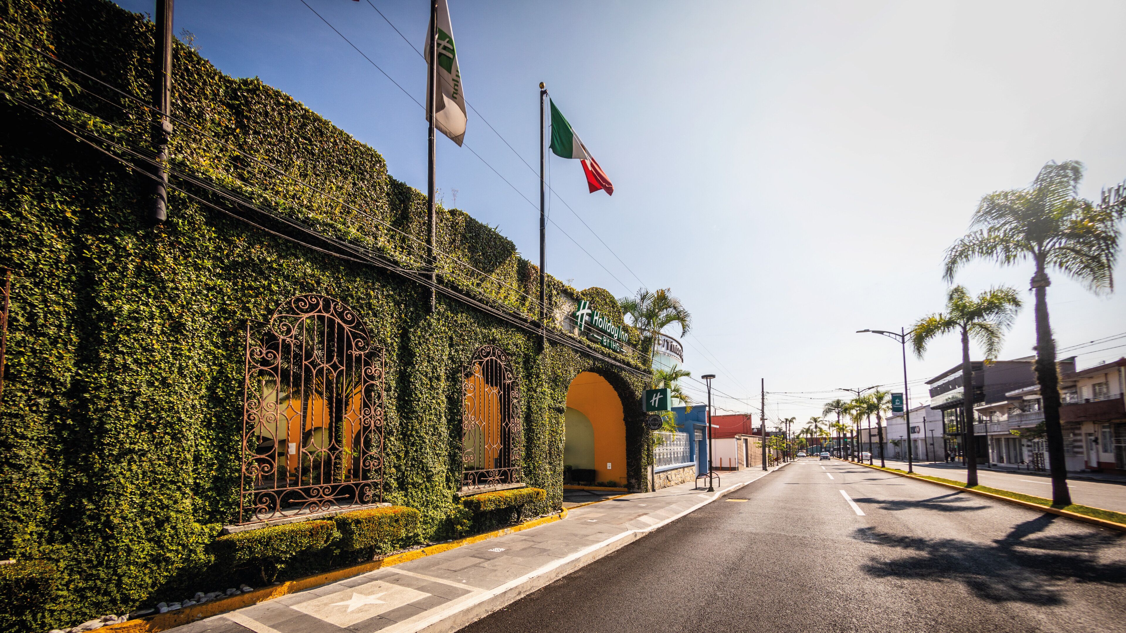 A building with a green ivy-covered facade, a gated entrance, and a sign for 'Holiday Inn'.