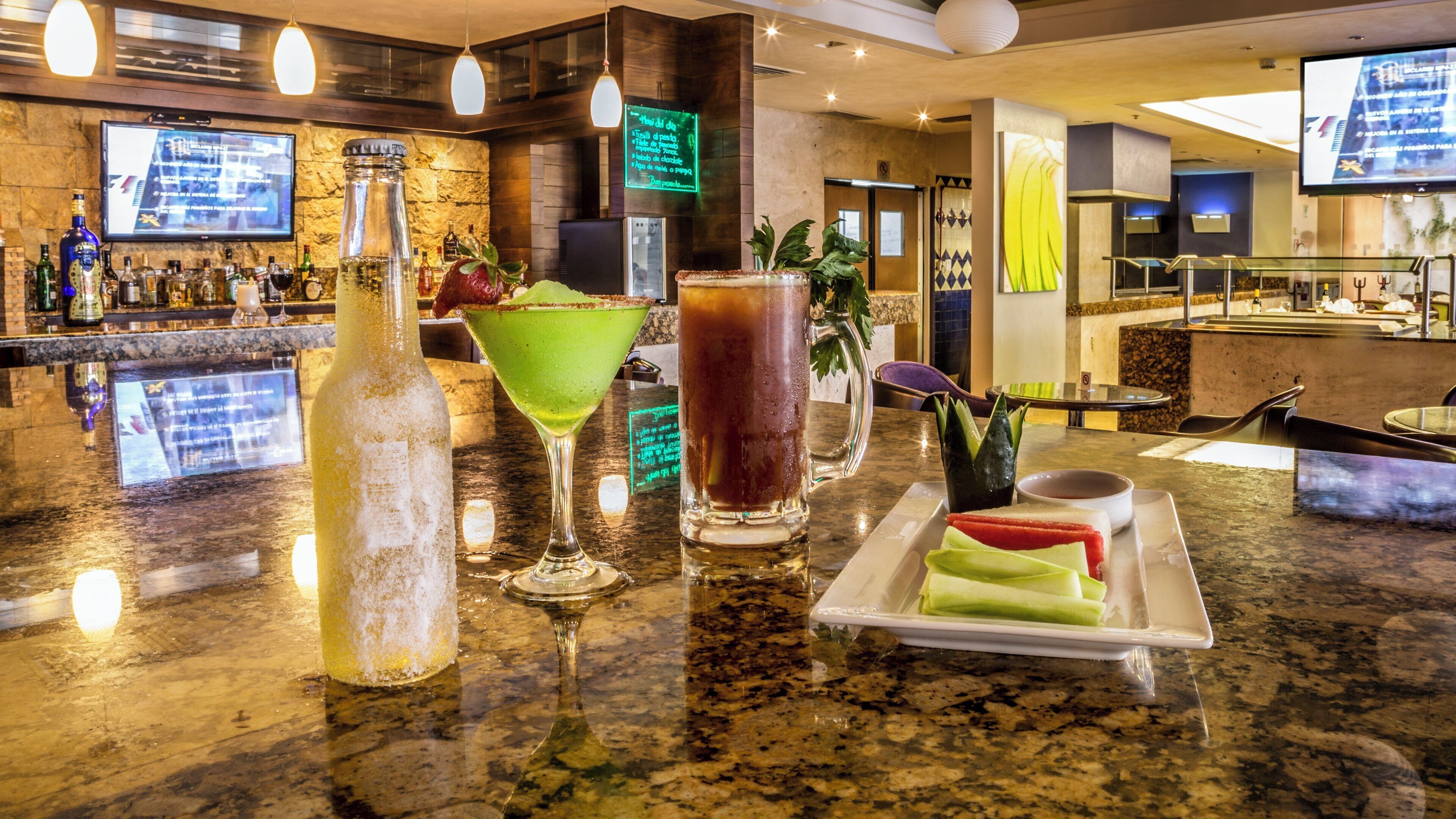 Una zona de bar con mostrador de granito, varias botellas, vasos y un tablero de menú.