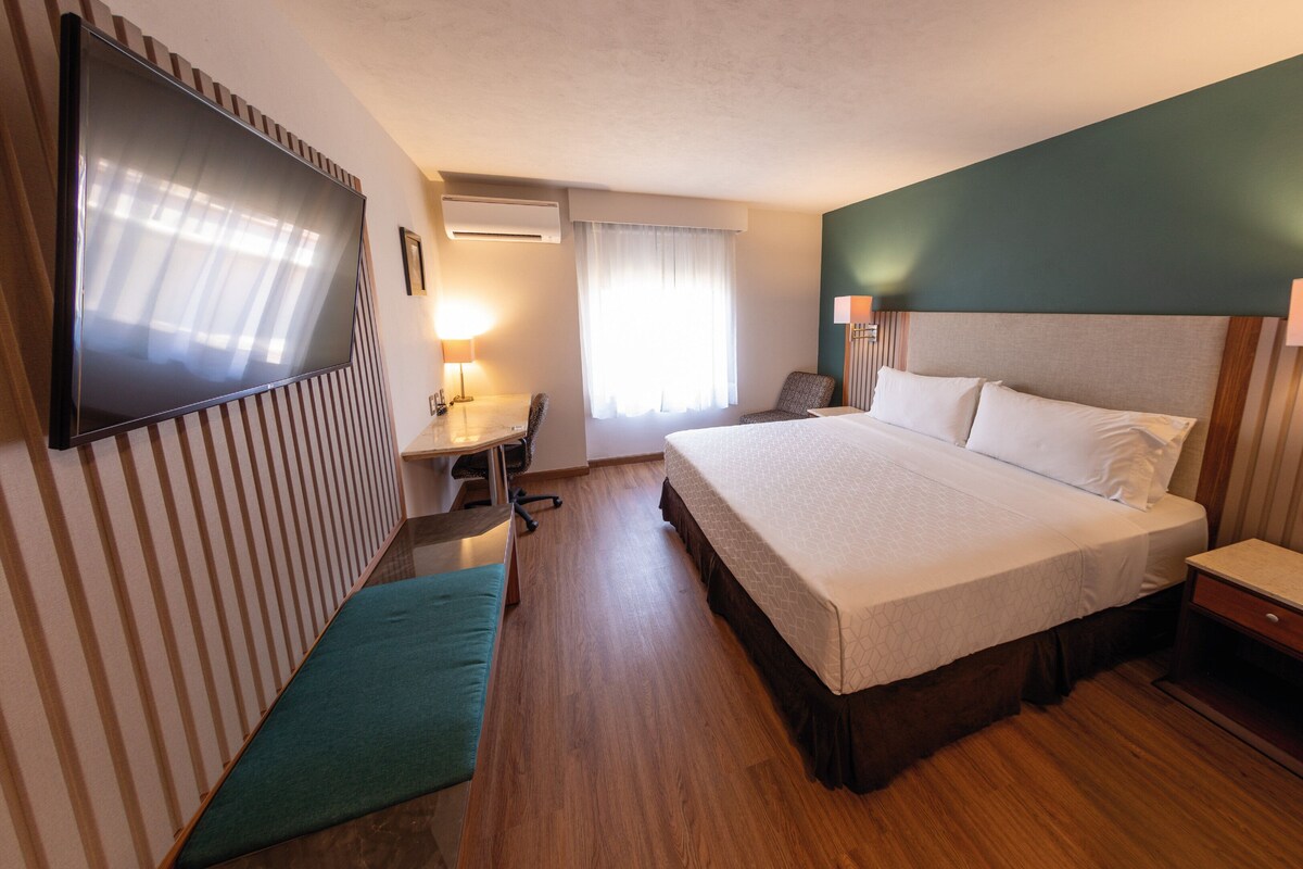 Una habitación de hotel con una cama grande, un escritorio, una silla, un televisor y un aire acondicionado.