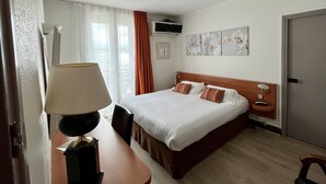 A hotel room with a bed, a desk, a chair, a lamp, a TV, and artwork on the wall. - Hotel Colbert (Saint-Jean-de-Luz)