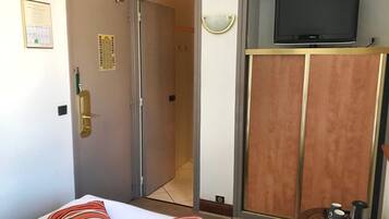 Habitación de hotel con una cama, un televisor sobre un mueble, una puerta con cerradura y una mesita con cafetera y tazas.