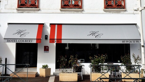 A hotel with red shutters on windows, a white facade, and a sign reading "HOTEL COLBERT". - Hotel Colbert (Saint-Jean-de-Luz)