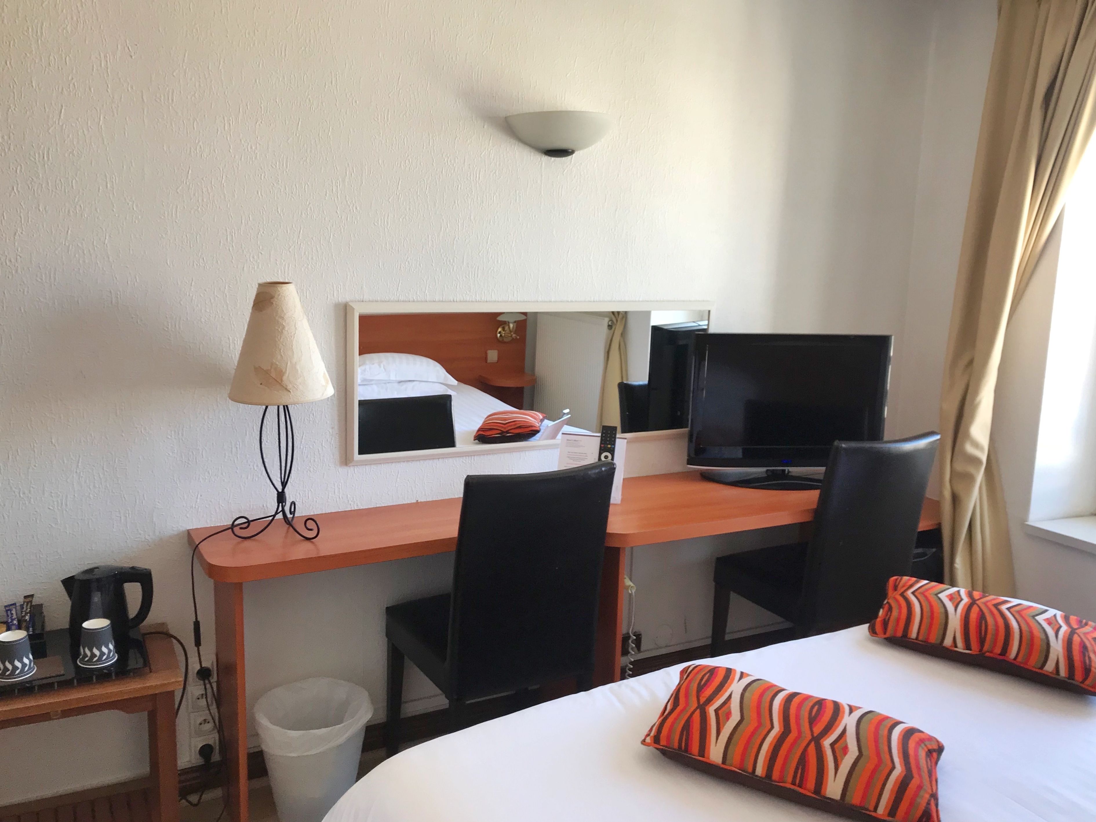 Una habitación de hotel con una cama, un escritorio con computadora, una lámpara y una silla.