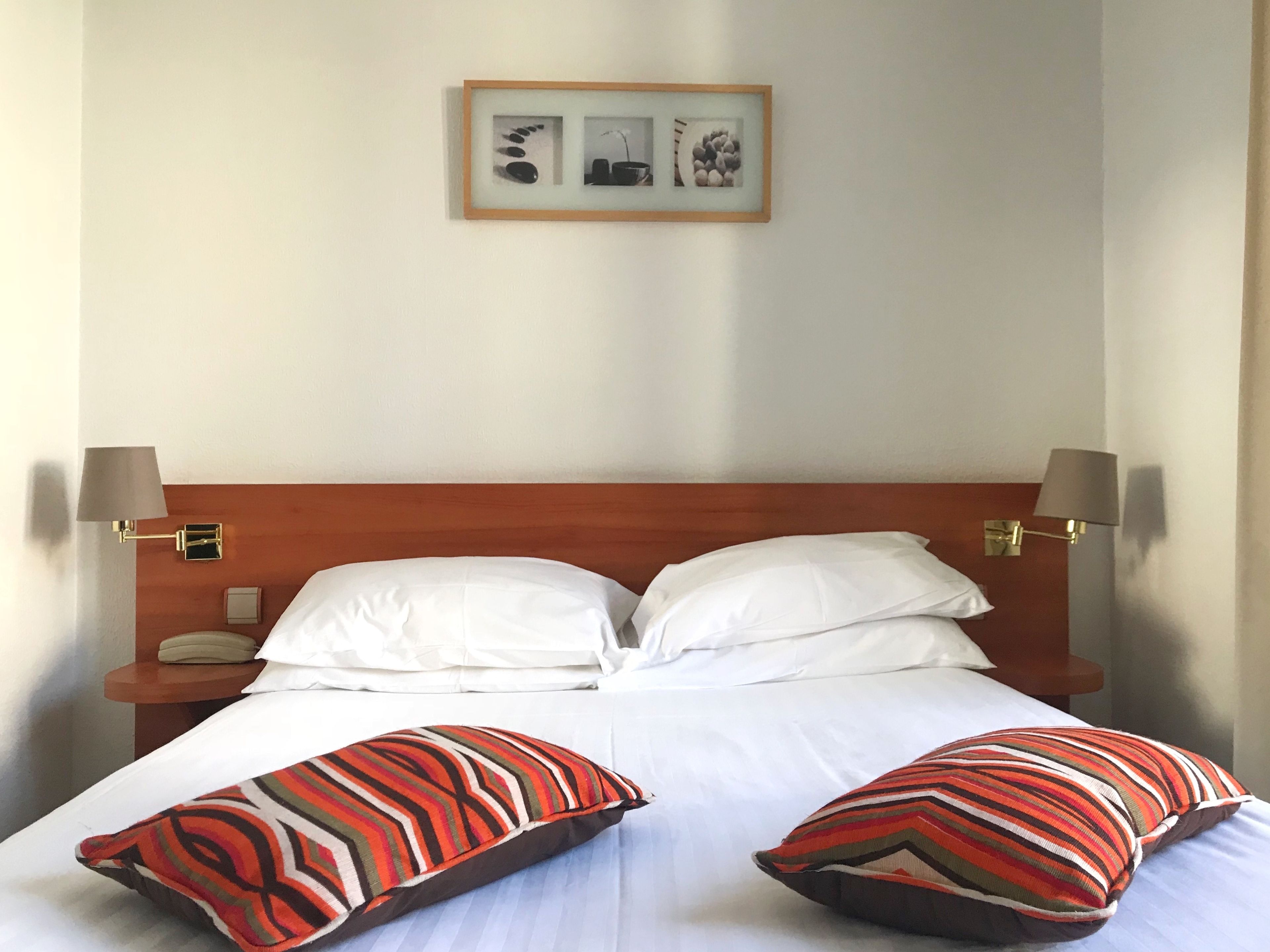 A neatly made bed with white linens, two striped pillows, and a framed picture above it.