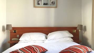 A neatly made bed with white linens, two striped pillows, and a framed picture above it.