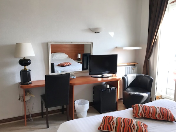 A hotel room with a bed, a desk with a computer, a chair, a TV, and a lamp.