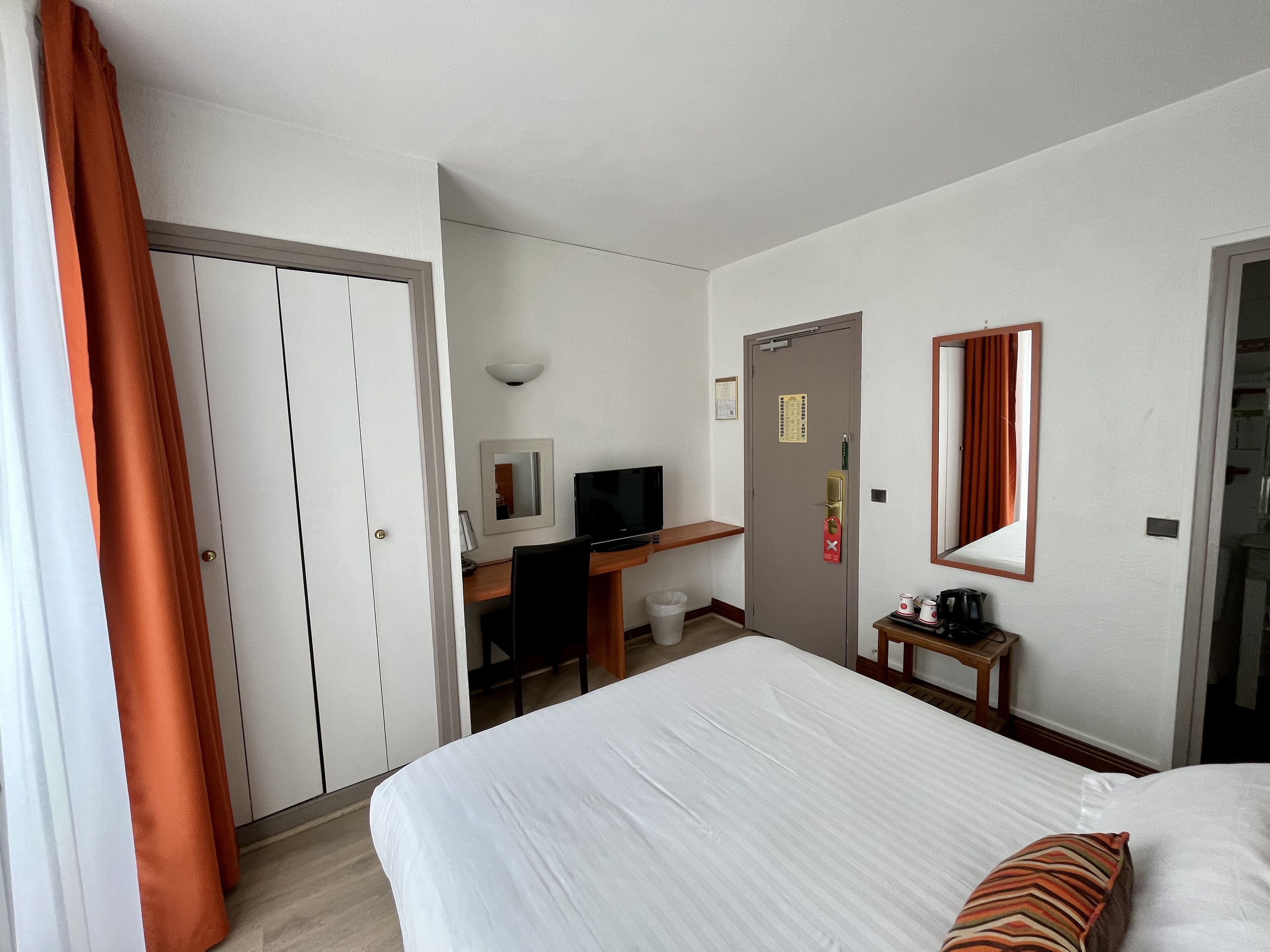 Habitación de hotel con cama, escritorio, computadora, televisor y armario.