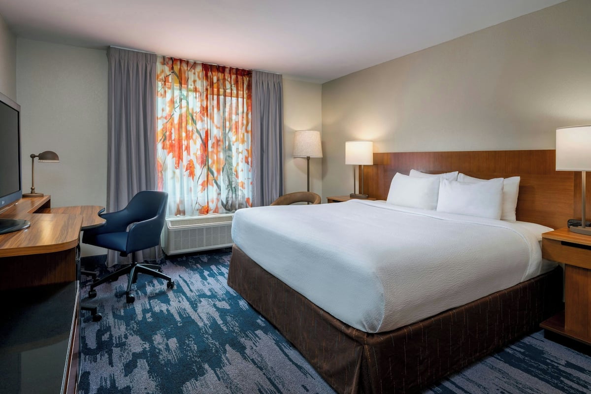 A hotel room with a large bed, a desk with a computer, a chair, and two lamps.