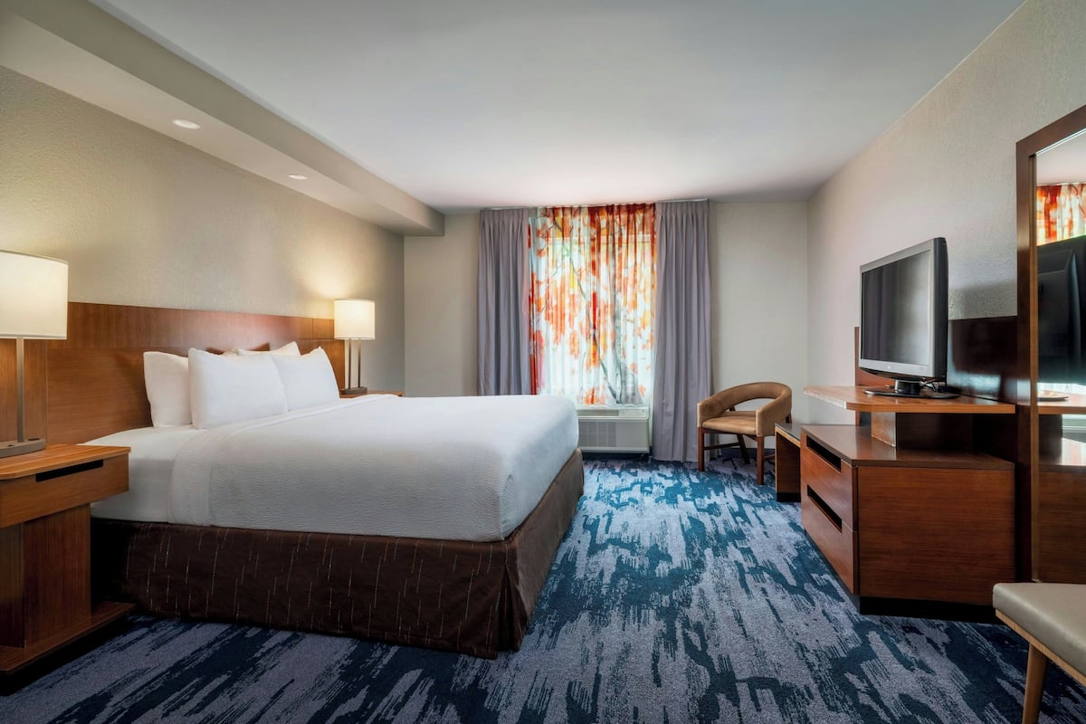A hotel room with a large bed, a desk with a television, a chair, and a window with curtains.