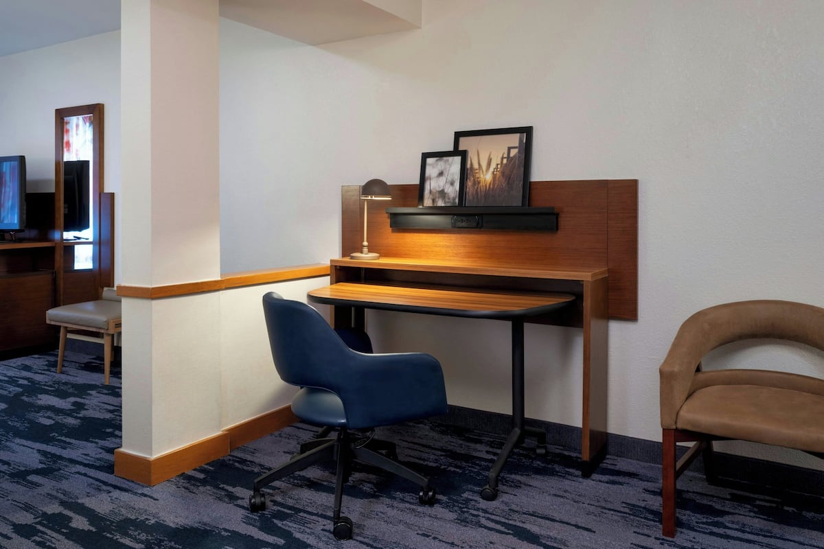 A hotel room with a desk, two chairs, a television, and a framed picture on the wall.