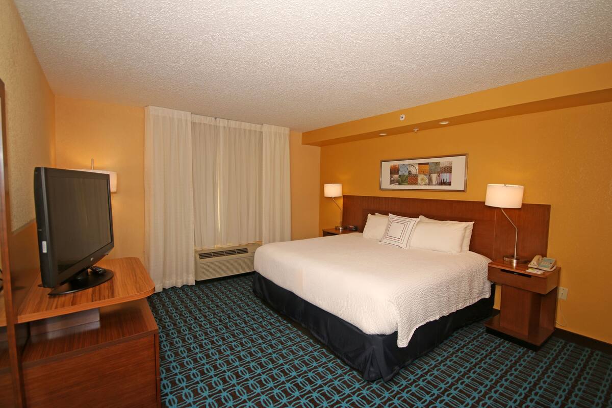 A hotel room with a large bed, a television on a wooden stand, two bedside lamps, and a framed picture on the wall.