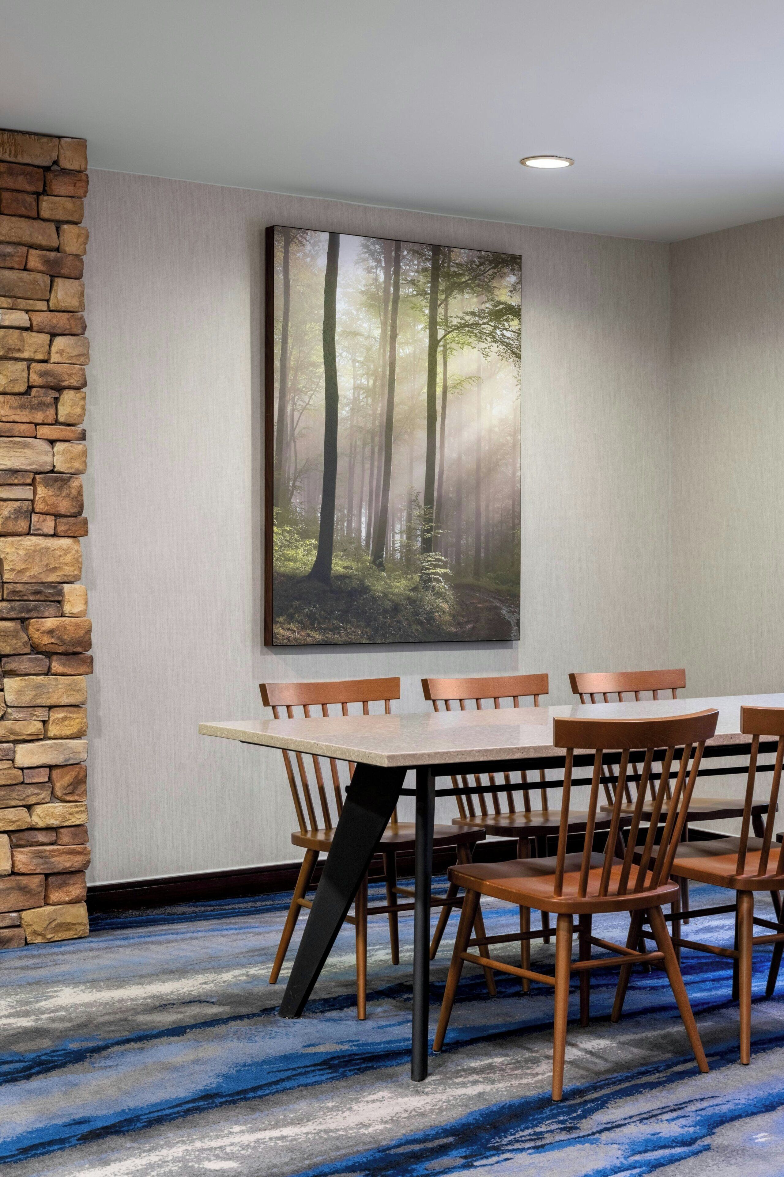 Un comedor con una pared de acento de piedra, un cuadro de gran tamaño con temática forestal y una alfombra de diseño azulado.