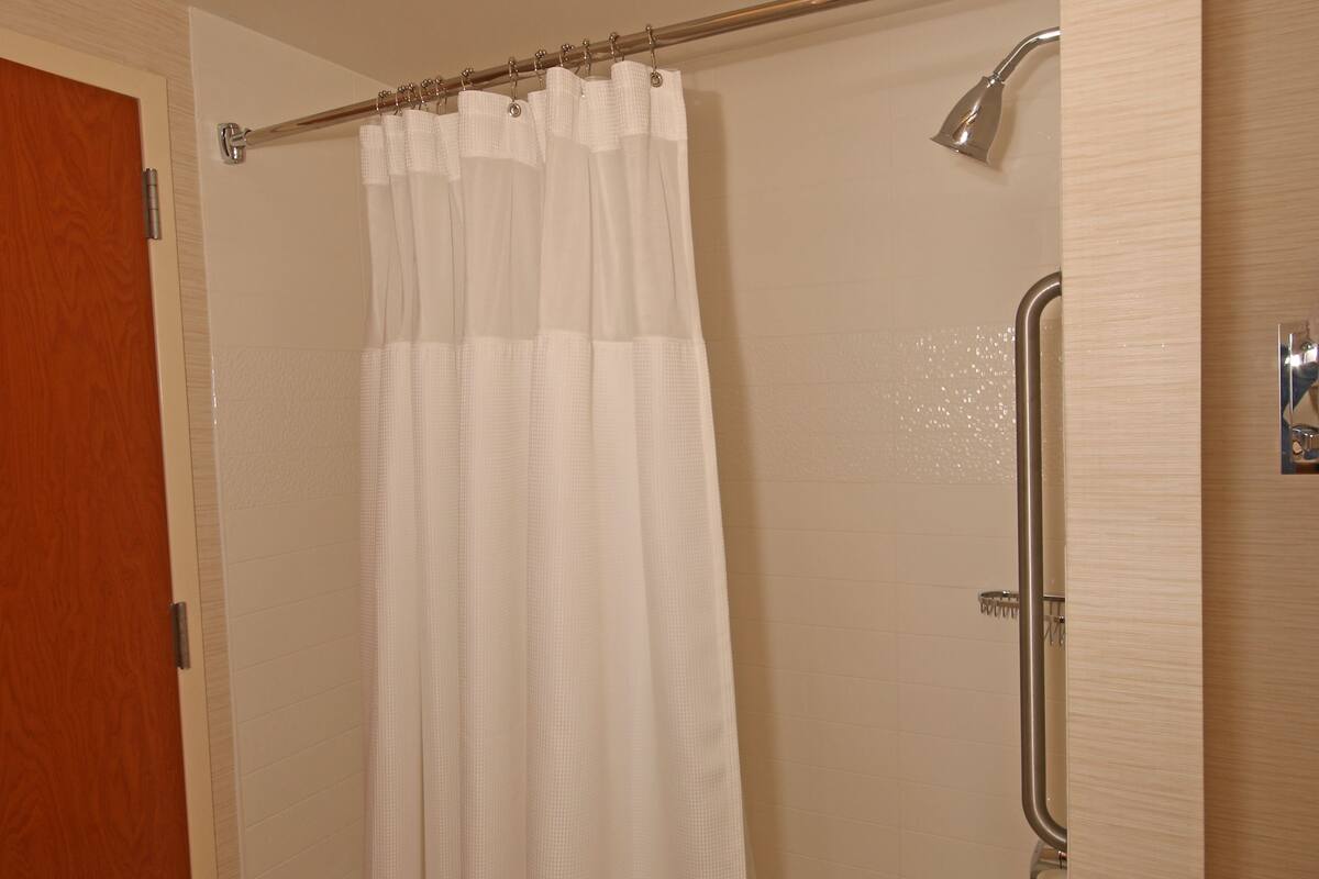 A bathroom with a shower, a glass door, and a white shower curtain.