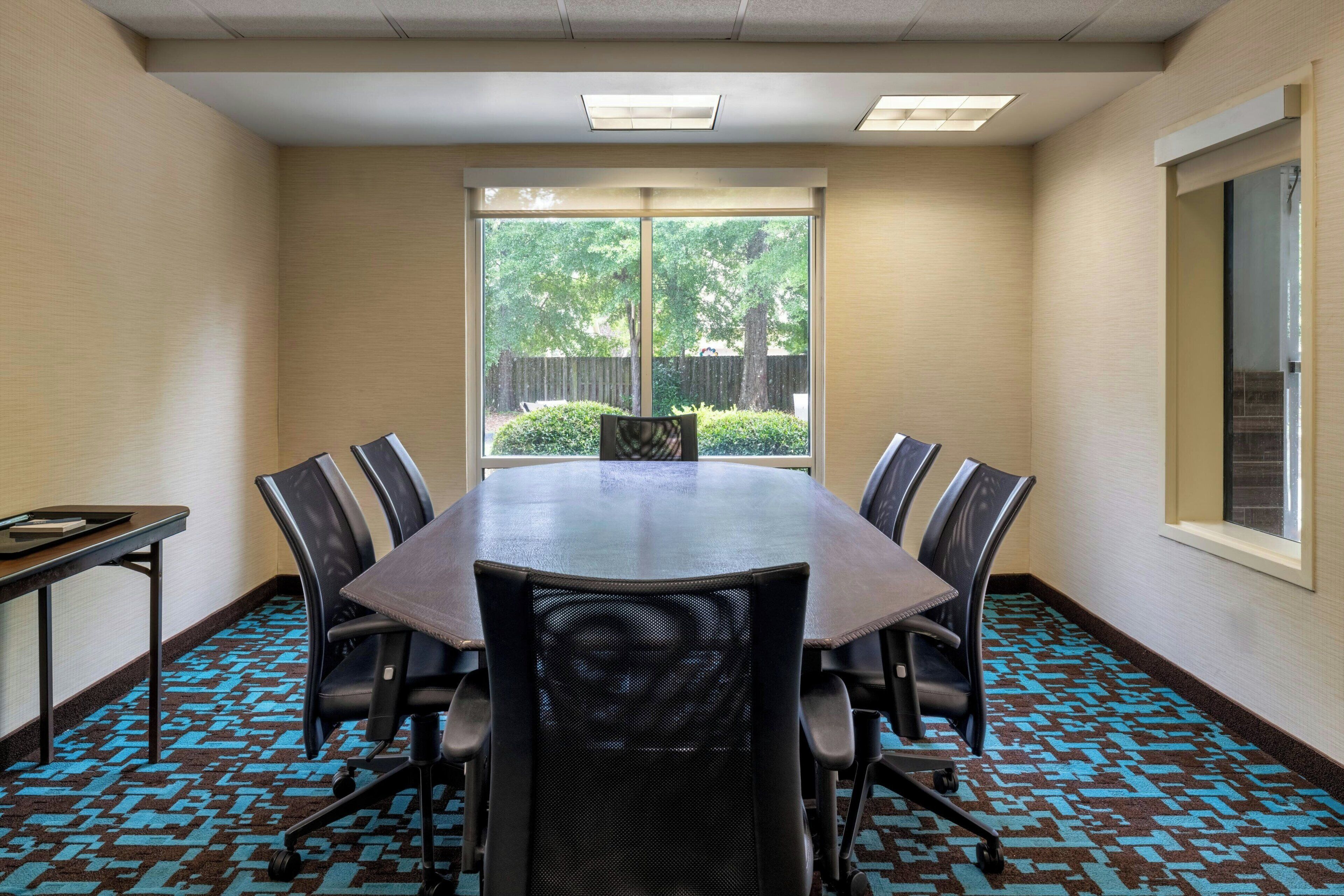 Une salle de conférence dotée d’une grande table, de six chaises et offrant une vue sur l’extérieur grâce à une grande fenêtre.