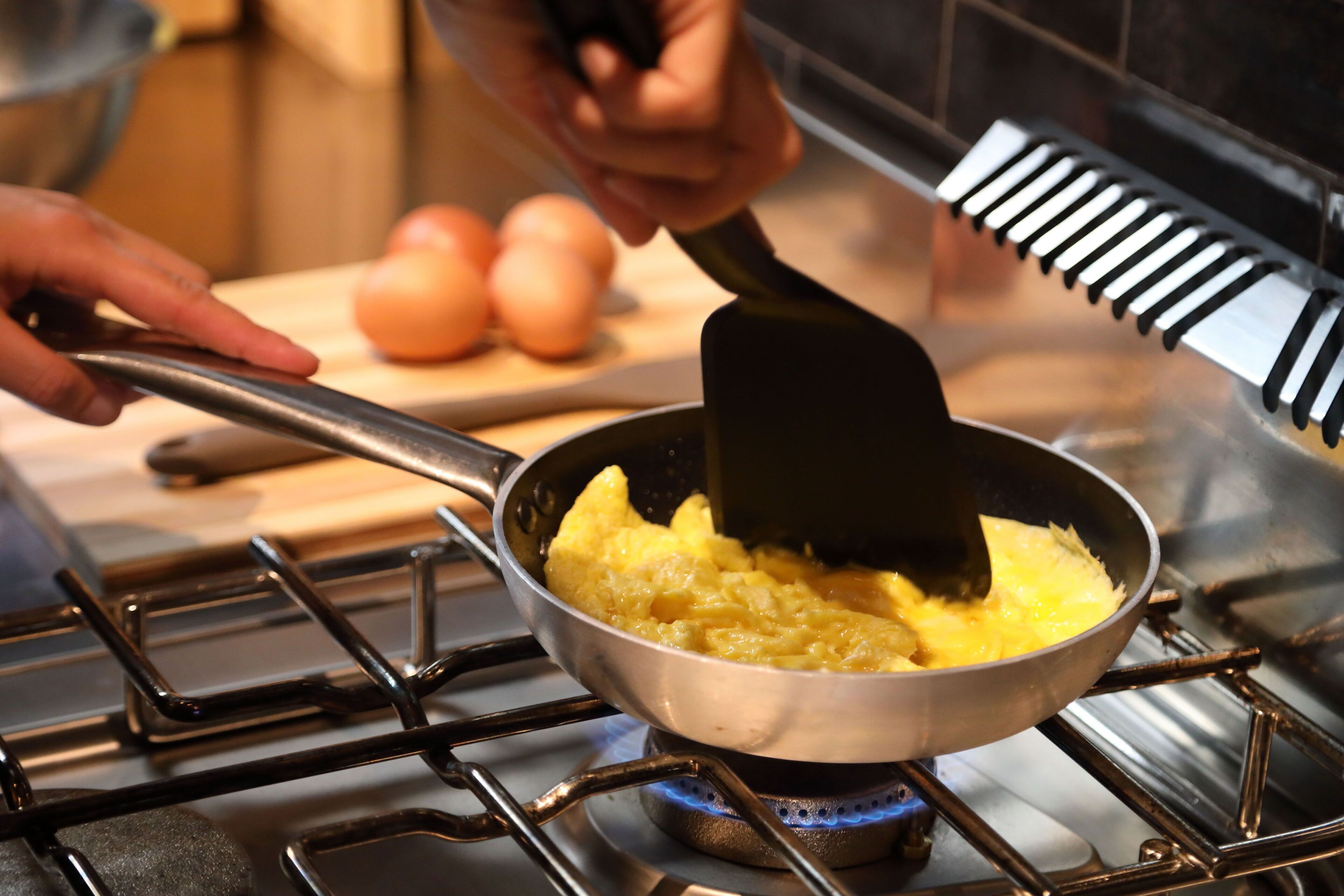 A person cooking scrambled eggs in a pan on a stove.