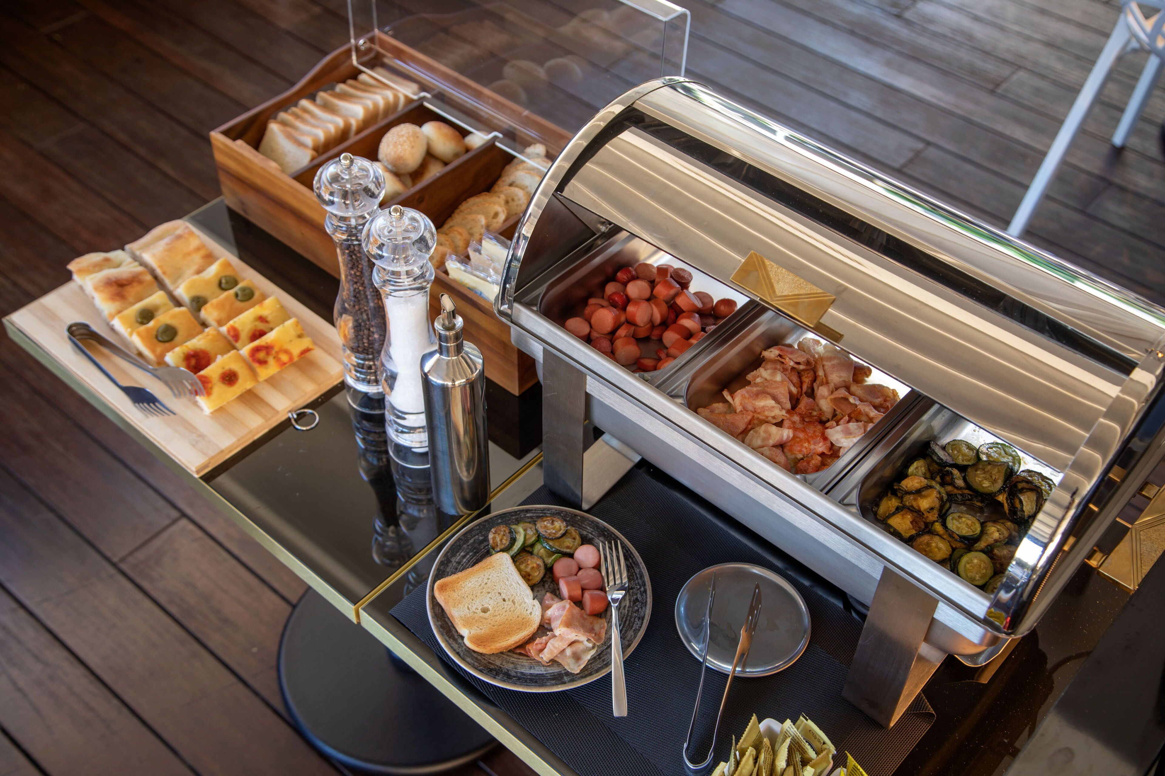 A buffet setup with various food items, including bread, pastries, and hot dogs.