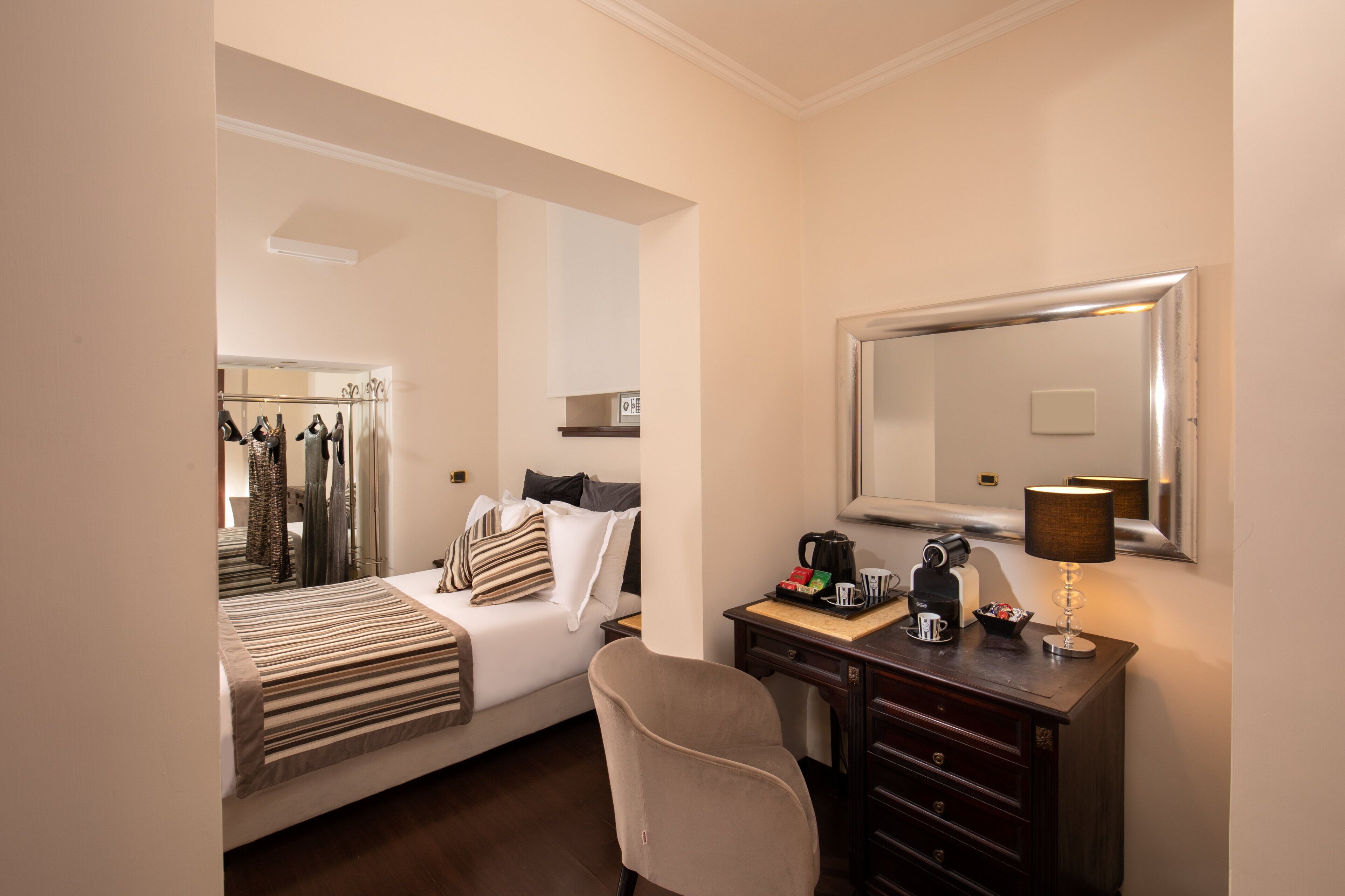 Quarto de hotel com uma cama, uma escrivaninha com luminária, um espelho e um guarda-roupa.