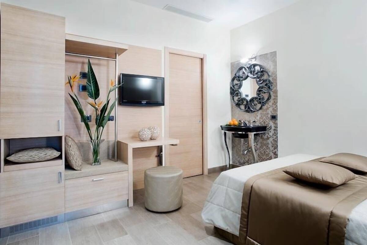 A modern bedroom with a bed, a TV, a vanity, and a decorative wall piece.